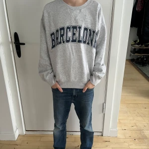 Grå barn sweatshirt från H&M med Barcelona-tryck - Säljer en grå sweatshirt från H&M med trycket “Barcelona” i storlek 165/88A. Tröjan har en klassisk rund halsringning och ribbade detaljer vid ärmslut och nederkant. Materialet är mjukt och bekvämt, perfekt för vardagsbruk.  Skick: Bra begagnat skick, med minimalt slitage. Nypris: 200 SEK  Modellen på bilderna är 160 cm lång, 12 år och har en smal/normal kroppsbyggnad.