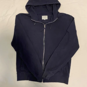 Mörkblå hoodie från Primark - Säljer en mörkblå hoodie från Primark i storlek L men sitter mer som M. Den har en dragkedja framtill och en praktisk huva med dragsko. Perfekt för en avslappnad stil.