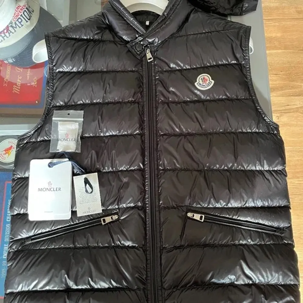 Snygg svart dunväst från Moncler med dragkedja och två fickor framtill. Perfekt för kyligare dagar och ger en stilren look. Moncler-logga på bröstet.. Takit.