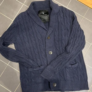 Mörkblå Cardigan från victor - Snygg mörkblå stickad kofta från Victor som är  kabelstickad. Skick 8/10. Han på bilden är 183 cm 70 kg. inga defekter!