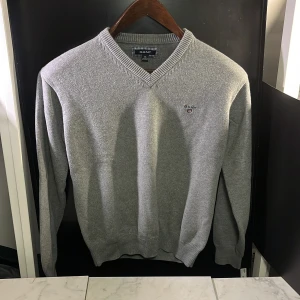 Grå tröja från GANT - Säljer en stilren grå tröja från GANT med v-ringning och ribbade muddar. Perfekt för en klassisk och bekväm look. Tröjan har en liten broderad logga på bröstet. Hör av er vid minsta fundering🙌