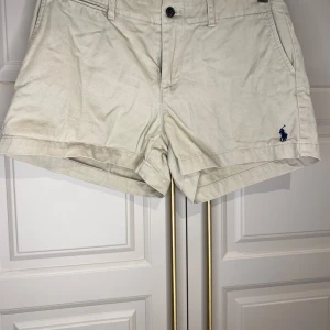 Beige shorts från Ralph Lauren Sport - Snygga beige shorts från Ralph Lauren Sport i 100% bomull. De har en klassisk design med knapp och dragkedja framtill samt två fickor bak med knappar. Perfekta för en avslappnad stil.