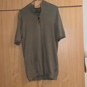 Beige kortärmad tröja med dragkedja - Säljer en stilren beige tröja med korta ärmar och dragkedja vid halsen. Perfekt för en avslappnad look. Tröjan har ribbade kanter vid ärmslut och nederkant.