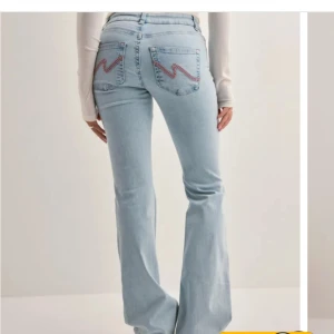 Ljusblå bootcut jeans med slitningar från nelly - Snygga ljusblå bootcut jeans med slitningar på knäna och coola broderade detaljer på bakfickorna. Perfekta för en avslappnad stil med en touch av edge.