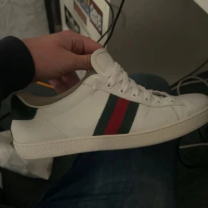 Vita sneakers med gröna och röda detaljer - Snygga vita sneakers från Gucci med klassiska gröna och röda ränder på sidan. Skorna har en grön häl med textur och märkets logotyp. Perfekta för en stilren look. Gucci påse tillkommer till skorna! NYPRIS 8000kr