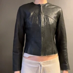 Svart skinnjacka från GAP - Snygg svart skinnjacka från GAP i äkta läder. Jackan har en stilren design med dragkedja framtill och långa ärmar. Perfekt för en cool och tidlös look.