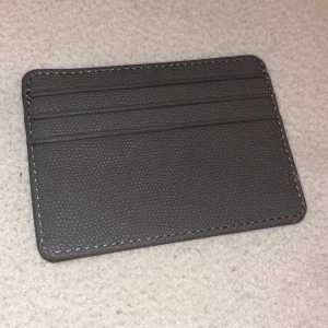 Grå plånbok i skinn - Säljer en stilren grå plånbok i skinn med plats för flera kort. Den har en praktisk fönsterficka på ena sidan för ID eller körkort. Perfekt för att hålla ordning på dina kort i en kompakt design.