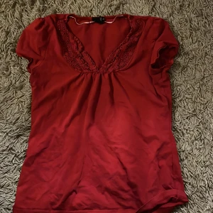 Röd topp med spetsdetaljer - Säljer en röd topp från H&M med v-ringning och blommiga spets detaljer