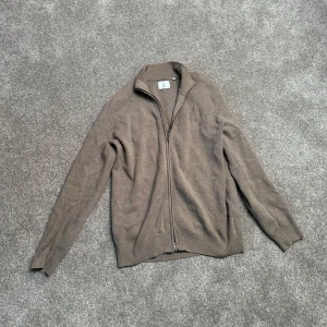 Beige kofta från Bläck - Säljer en stilren beige kofta från Bläck med dragkedja framtill. Perfekt för lager-på-lager under kyligare dagar. Koftan har långa ärmar och en klassisk krage. Storlek M.