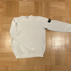 Vit sweatshirt från Stone Island - Säljer en stilren vit sweatshirt från Stone Island. Tröjan har en klassisk rund halsringning och en ikonisk logga på ärmen. Perfekt för en avslappnad och trendig look. Passar dig om du är längre. Själv är jag runt 167 och den har passat mig ganska bra 