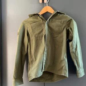 Grön skjorta från Arket - Säljer en grön skjorta från Arket i ekologisk bomull. Skjortan har långa ärmar och två bröstfickor med knappar. Perfekt för en stilren och avslappnad look. Använd ett fåtal gånger du den har blivit för liten👍