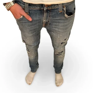 Nudie jeans med slitningar - Tja säljer nu dessa feta jeans från nudie med slitningar. Dem är i storlek 29/32 och passar dig runt 180, modellen är 180cm lång. Dem har en liten defekt som är ett hål över fickan där bak(se bild 3)  men inget som riktigt syns när man använder dem samt vilket också går att laga rätt lätt. 