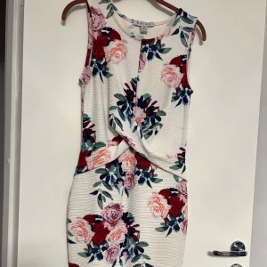 Blommig ärmlös klänning från New Look - Säljer en somrig och blommig klänning från New Look. Den är ärmlös med ett vackert blommönster i rosa, rött och grönt på en vit bakgrund. Perfekt för varma dagar!