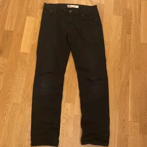 Svarta Levis 502 Regular Taper jeans - Snygga svarta Levis 502 Regular Taper jeans med en klassisk design. De har en normal passform med avsmalnande ben och är perfekta för en stilren look. Byxorna har fem fickor och knappar i midjan.