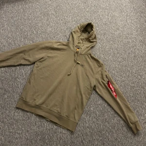Alpha Industries hoodie - Grön / khaki hoodie från Alpha Industries med klassiska tag:en på ärmen. Storlek är M. Enbart använd 2 gånger, i helt felfritt skick. Pris går att diskutera vid snabb affär