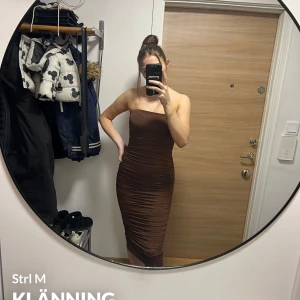 Brun axelbandslös klänning från Zara - Snygg brun axelbandslös klänning från Zara i en tight passform. Perfekt för en kväll ute eller en speciell tillställning. Klänningen har en elegant drapering som ger en smickrande silhuett. Tillverkad i ett mjukt och stretchigt material för bästa komfort.