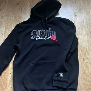 Svart hoodie från Supply & Demand - Säljer en svart hoodie från Supply & Demand med tryck på framsidan. Hoodien har en klassisk design med känguruficka och justerbar huva. Perfekt för en avslappnad stil.