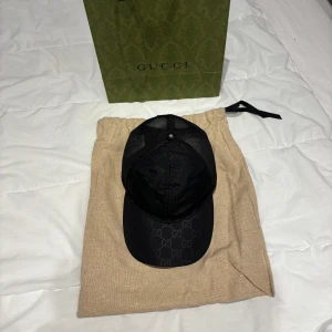Svart keps från Gucci - Snygg oandvänd, svart keps från Gucci med det ikoniska GG-mönstret. Kepsen har en nätpanel baktill för bättre ventilation och en justerbar rem för perfekt passform. Perfekt för att ge en lyxig touch till din outfit.