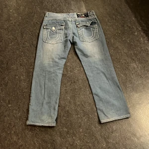 Blå jeans från True Religion - Snygga blå jeans från True Religion med klassisk femficksdesign och kontrastsömmar. Byxorna har en normal passform och är tillverkade i USA. Perfekta för en avslappnad stil.