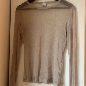 Beige glittrig topp från Gina Tricot - Säljer en snygg beige glittrig topp från Gina Tricot. Toppen har långa ärmar och är perfekt för att lägga till lite glitter i din outfit. Den är i storlek M och passar bra för festliga tillfällen.