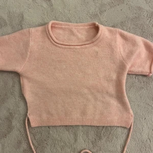 Rosa croppad topp med knytband - Säljer en söt rosa croppad topp med korta ärmar och knytband i midjan. Perfekt för en avslappnad stil. Toppen är gjord i ett mjukt material som känns skönt mot huden.