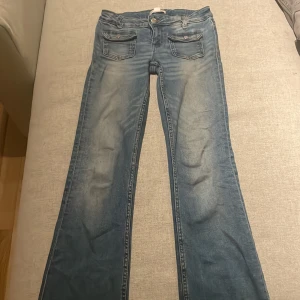 Blå jeans från Gina Tricot - Säljer ett par snygga blå jeans från Gina Tricot i storlek 152. De har en klassisk femficksdesign med knappar och dragkedja framtill. Jeansen har en lätt slitning för en trendig look.
