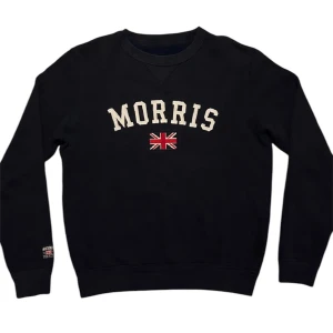 Svart sweatshirt från Morris - Snygg svart sweatshirt från Morris med broderad logga och brittisk flagga på bröstet. Tröjan har långa ärmar och rund halsringning. Perfekt för en stilren och avslappnad look.