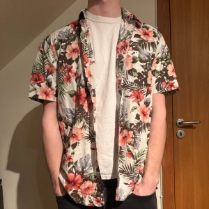 Blommig kortärmad skjorta från East West - Säljer en färgglad blommig skjorta från East West. Modellen är 183cm och bär storleken L. Hör av dig vid fråga. 