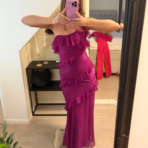 Lila axelbandslös klänning med volanger - Säljer en fantastisk lila axelbandslös klänning med volanger. Den har en figurnära passform och är perfekt för bal eller andra speciella tillfällen. Klänningen är lång och har en elegant design som verkligen sticker ut. 