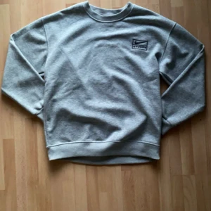 Grå sweatshirt från Nike x Stussy - Säljer en stilren grå sweatshirt från Nike i samarbete med Stussy. Tröjan har en broderad logga på bröstet och är tillverkad i mjukt material för extra komfort. Perfekt för en avslappnad look.