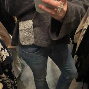 Glittrig axelväska - Säljer en glittrig axelväska med en smidig axelrem. Väskan har en knappdetalj på framsidan och är perfekt för att bära med sig det nödvändigaste. Den glittriga ytan ger en festlig touch till din outfit.