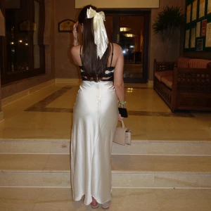 Vit långklänning med svarta spetsdetaljer - Elegant vit långklänning med svarta spetsdetaljer och smala axelband. Klänningen har en v-ringad design och en slits framtill. Köpt från Gina tricot storlek XS men passar även S. använd endast 1 gång säljer då den är för liten för mig nu 