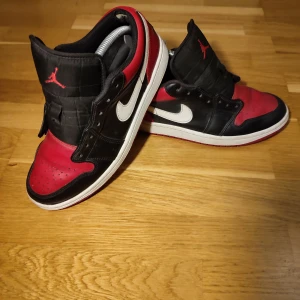 Nike Air Jordans 1 - Säljer ett par klassiska Nike Air Jordans i rött och svart med vit sula. Skorna har snörning och den ikoniska Jumpman-loggan på plösen. Perfekta för sneaker-entusiaster!