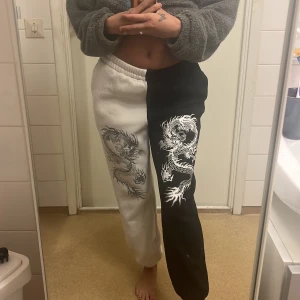 Svartvita mjukisbyxor med drakmotiv - Unika mjukisbyxor i svart och vitt med coolt drakmotiv på benen. Perfekta för en avslappnad stil med en twist. Byxorna har en bekväm passform och elastisk midja.