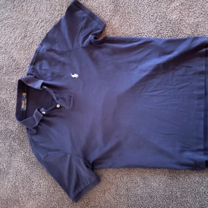 Mörkblå pikétröja från Ralph Lauren - Säljer en snygg och stilren mörkblå pikétröja från Ralph Lauren i storlek M. Den är i perfekt skick och har inga defekter.