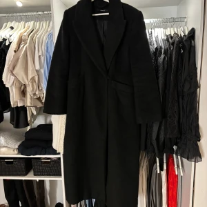 Svart kappa - Elegant svart kappa med klassisk design och långa ärmar. Perfekt för kyligare dagar och ger en stilren look. Passar bra till både vardag och mer formella tillfällen. Från Gina tricot storlek M