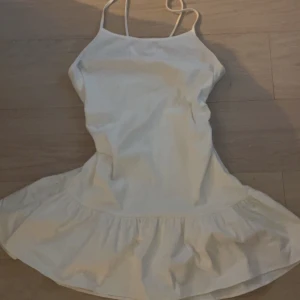 Vit ärmlös klänning med volang - Säljer en söt vit klänning med smala axelband och volangdetalj vid fållen. Perfekt för varma dagar och somriga tillfällen. Klänningen har en enkel och stilren design som gör den lätt att matcha med olika accessoarer.