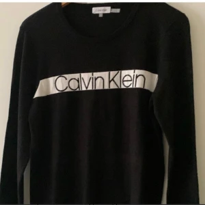 Svart tröja från Calvin Klein - Snygg svart tröja från Calvin Klein med deras ikoniska logga i vitt på bröstet. Tröjan har långa ärmar och en klassisk rund halsringning. Perfekt för en stilren look.