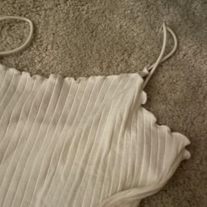 Vit ribbad klänning - Säljer en stilren vit ribbad klänning med smala axelband. Perfekt för en somrig look med sin lätta och luftiga design.