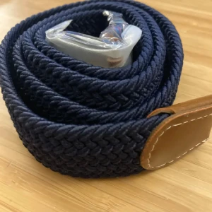 Blått flätat bälte med bruna skinn detaljer - Snyggt blått flätat bälte med bruna skinn detaljer och en silverfärgad spänne. Perfekt för att ge en stilren touch till din outfit. Passar både till jeans och chinos.
