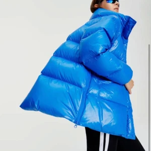 Blå pufferjacka från peak performance  - Snygg blå pufferjacka med hög krage och dragkedja. Jackan har en oversized passform och är perfekt för kalla dagar. Den quiltade designen ger extra värme och stil.