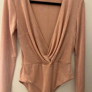 Beige omlott body från Gina Tricot - Snygg beige body från Gina Tricot med omlott-design och långa ärmar. Perfekt för en stilren look. Tillverkad i ett mjukt och stretchigt material som ger en bekväm passform.