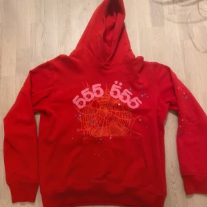Röd Sp5der Hoodie - Cool röd hoodie med unik spindelnätsdesign och siffrorna 555 i rosa på framsidan. Detaljer som små stjärnor och blixtar ger en extra touch. Perfekt för en avslappnad stil.