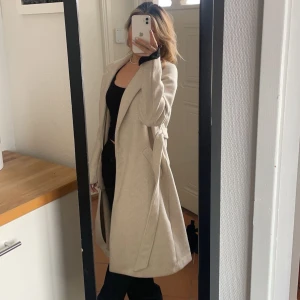 Beige kappa - Snygg beige kappa med lång passform och stilren design. Perfekt för höst och vår, med en klassisk look som passar till många tillfällen. Använd en del gånger, nopprig. 