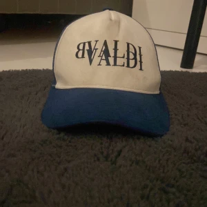 Vit och blå keps från BVALDI - Snygg keps från BVALDI i vit och blå färgkombination. Kepsen har en böjd skärm och justerbar passform baktill. Perfekt för en avslappnad stil.