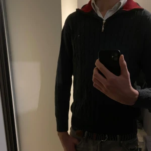 Mörkgrå tröja med dragkedja från Tommy Hilfiger - Snygg mörkgrå ribbad tröja från Tommy Hilfiger med dragkedja och krage. Tröjan är i 100% bomull, har ett diskret märke på bröstet och en röd insida vid kragen. Perfekt för kyligare dagar. Nypris ca 1000-1200 kr.