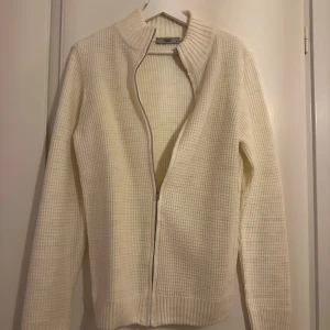 Vit stickad kofta med dragkedja - Säljer en stilren vit stickad kofta med dragkedja. Perfekt för kyliga dagar med sin ribbade struktur och långa ärmar. Enkel att matcha med olika outfits.