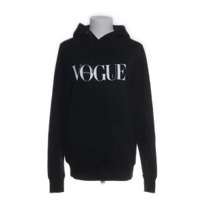 Svart hoodie med Vogue-tryck - Snygg svart hoodie med stort Vogue-tryck på framsidan. Tillverkad i 100% ekologisk bomull, perfekt för en stilren och bekväm look. Långärmad med klassisk huva.