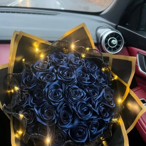 Evighetsbukett - En elegant bukett med mörkblå rosor, dekorerad med en varm ljusslinga som ger ett stämningsfullt sken. Perfekt som en unik present eller dekoration.
