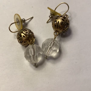 Guld- och kristall liknande örhänge  Vintage  - Eleganta örhängen med en gyllene kula och en klar kristallpärla. Perfekta för att ge en touch av glamour till din outfit. De har en krok för enkel användning.